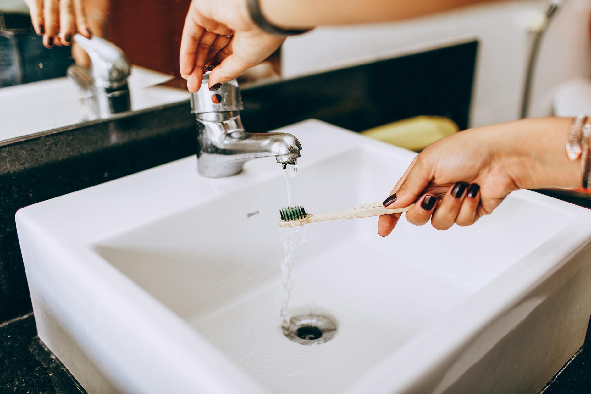 Woman Holding Toothbrush under Water in Sink