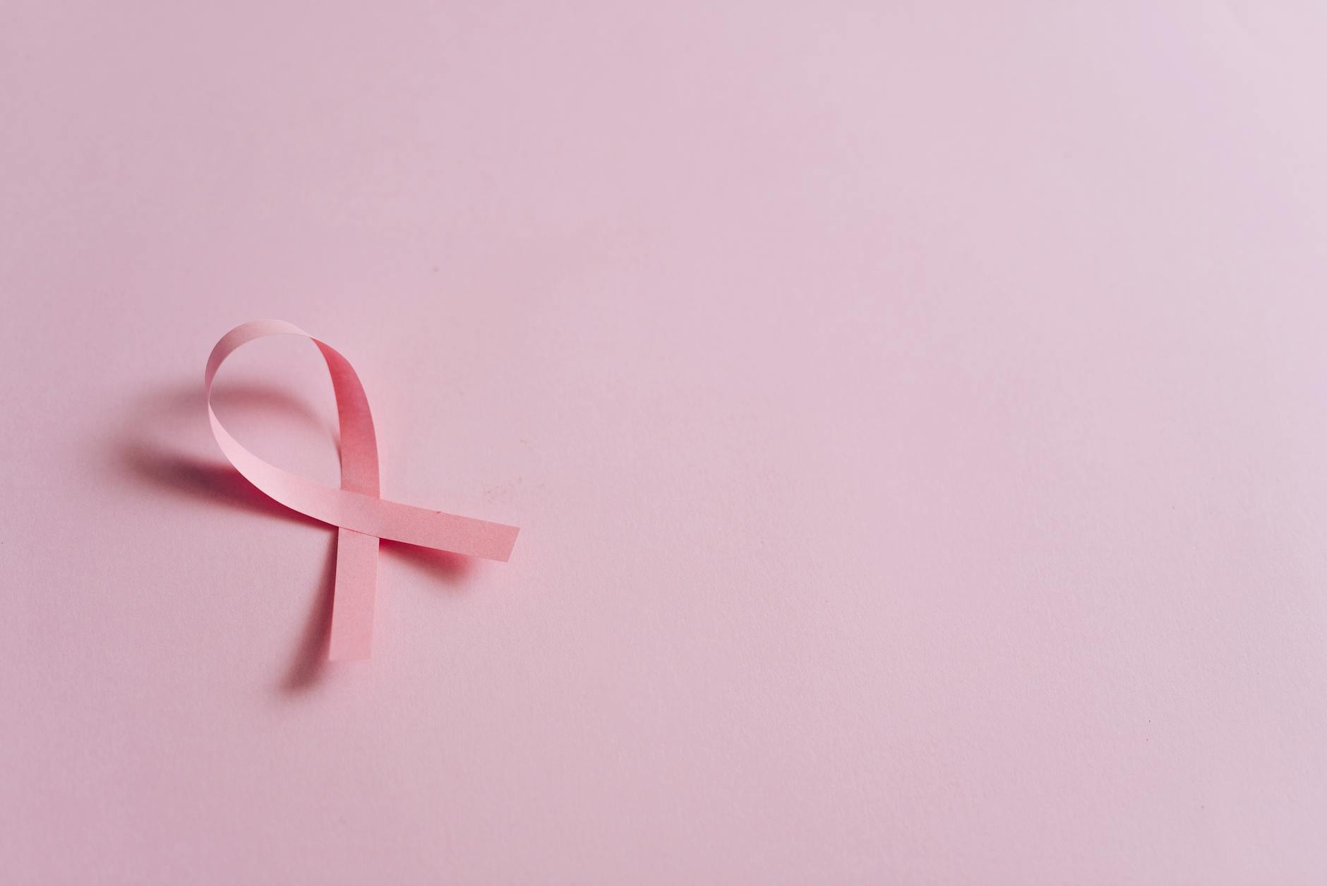 Minimalist pink ribbon symbolizing breast cancer awareness on a pink background.