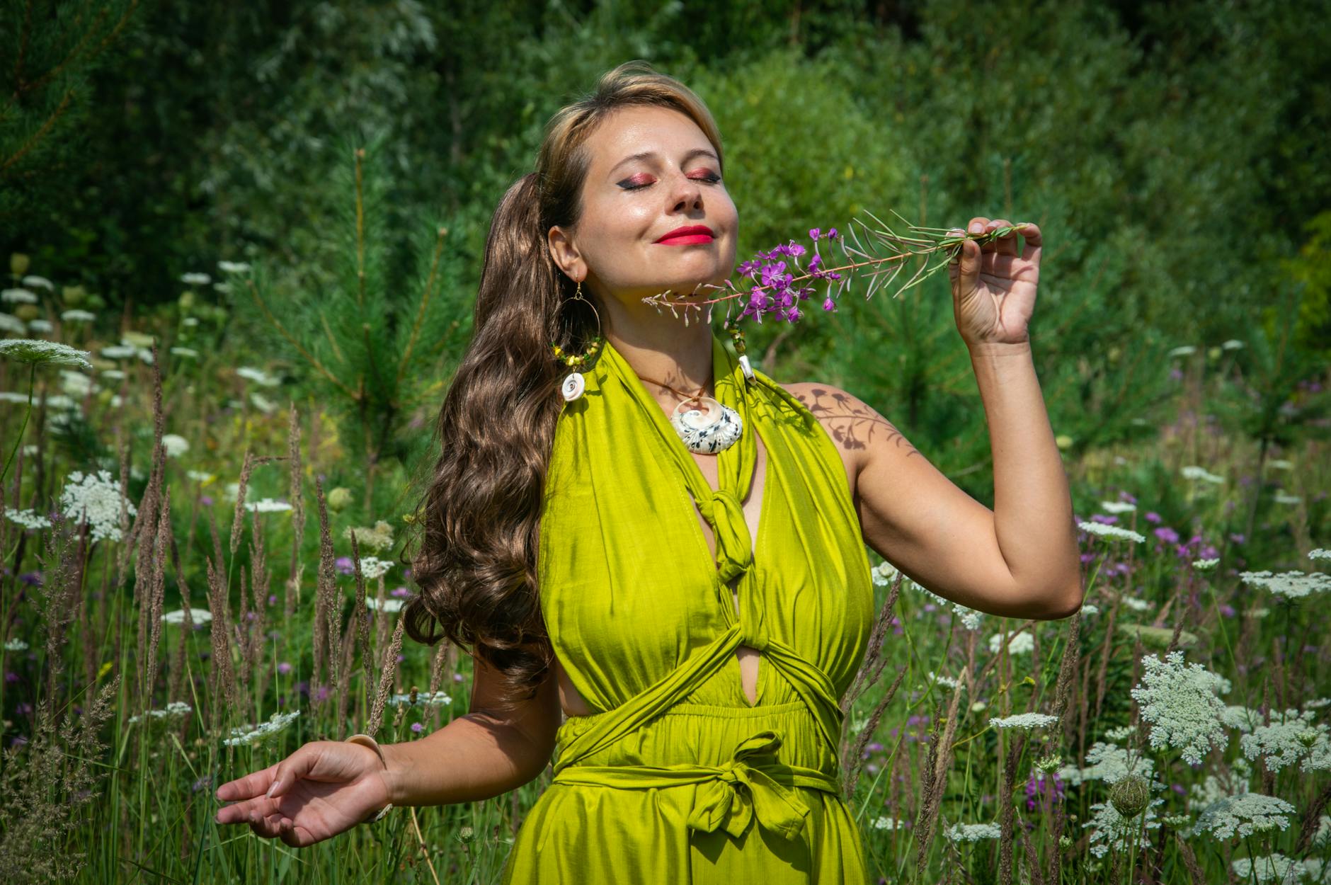 A woman in a green dress savoring wildflowers in a meadow on a sunny day.