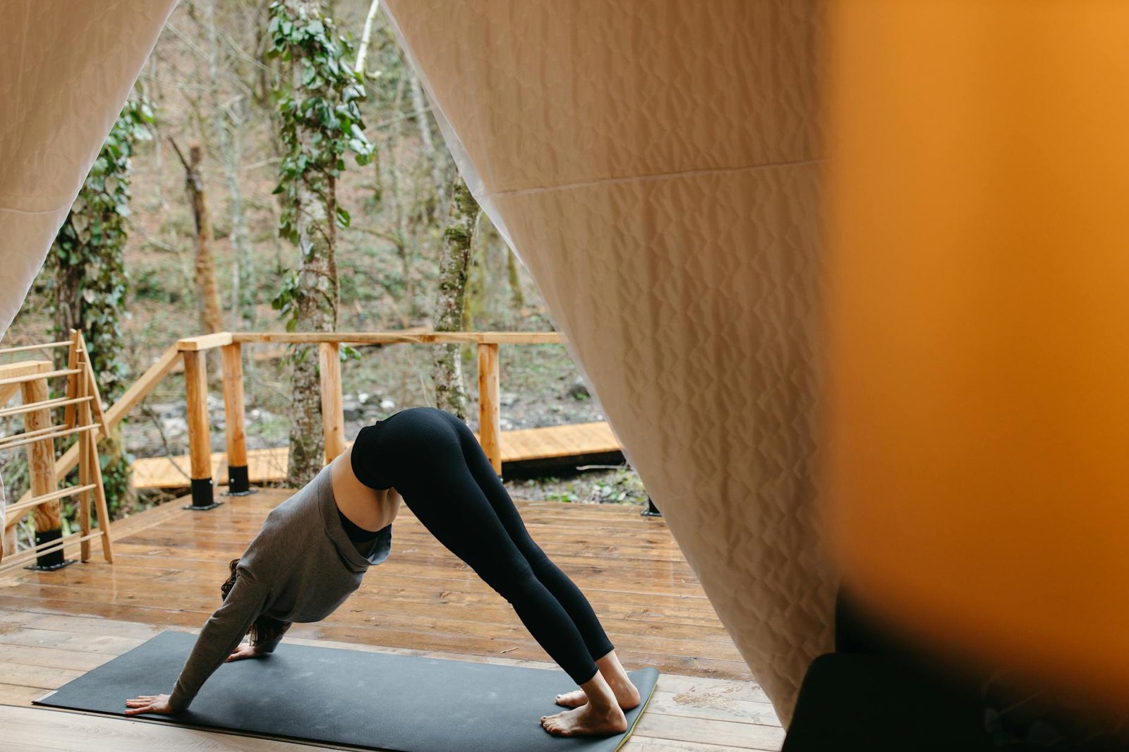Woman practicing yoga outdoors in a tent, emphasizing relaxation and fitness.